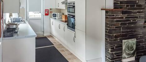 A compact kitchen with white cabinets, a microwave, an oven, and a stone fireplace.