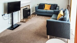 Een woonkamer met een flatscreen televisie, een open haard, een bank, een salontafel en een lamp.