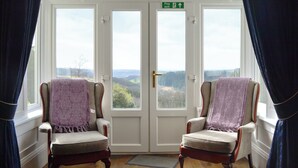A room with two armchairs facing a large window with a view of a landscape. There is a door with a fire exit sign above it.