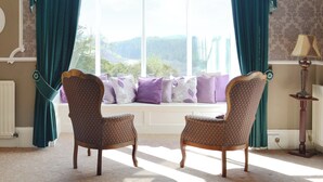 A room with two upholstered chairs facing a large window with curtains.