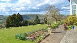A garden pathway leading to a building with a view of a valley and hills.