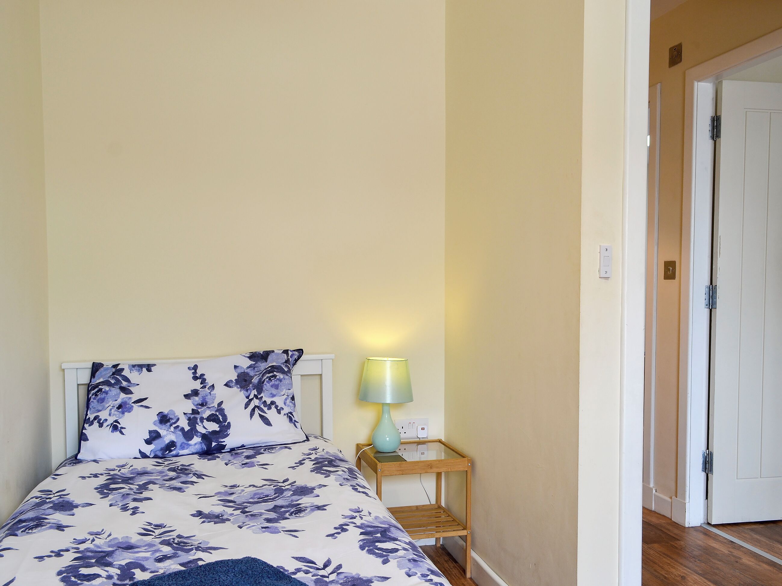 Uma cama com colcha florida, uma luminária de cabeceira e uma mesa de cabeceira de madeira.