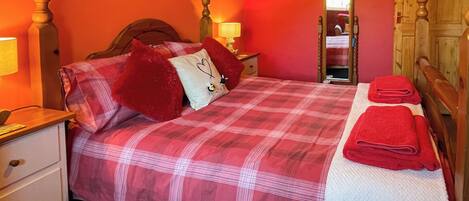 A bedroom with a bed, pillows, a nightstand, a dresser, a mirror, and a door.