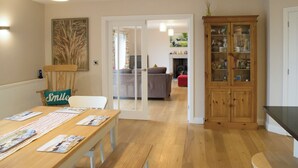 A dining area with a wooden table and chairs, a cabinet with glass doors, and a doorway leading to another room. - Perfect for families wanting to holiday together. (Marhamchurch, near Bude)