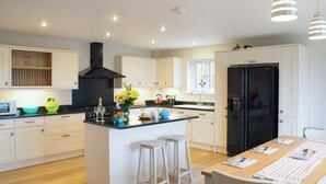 A modern kitchen with white cabinetry, a black stove, and a central island with stools. - Perfect for families wanting to holiday together. (Marhamchurch, near Bude)