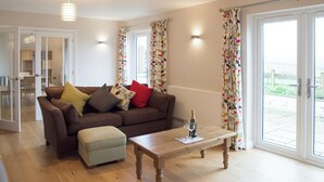 A living room with a brown sofa, ottoman, and wooden coffee table. - Perfect for families wanting to holiday together. (Marhamchurch, near Bude)