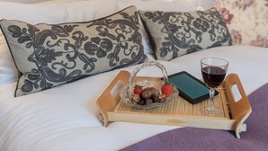 A bed with white linens, two decorative pillows, a tray with chocolates and strawberries, a glass of red wine, and a book. - Brewery House Cottage (Bishop Middleham, near Durham)