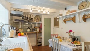 A cozy kitchen with a dining area, featuring a sink, cabinets, a clock, and a table set for breakfast. - Brewery House Cottage (Bishop Middleham, near Durham)