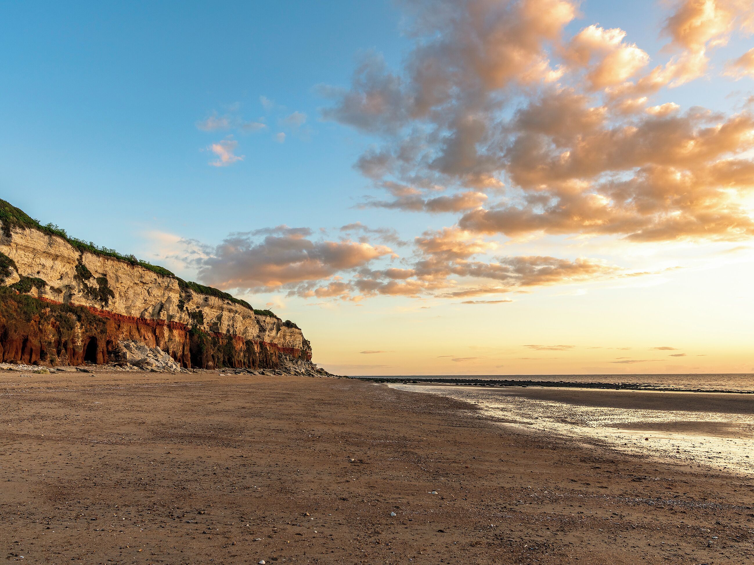 Un paisaje costero con una playa de arena, acantilados y cielo despejado.