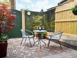 A patio with two wicker chairs and a table, a potted plant, and a wooden fence. - 1 bedroom accommodation in Hunstanton (Hunstanton)