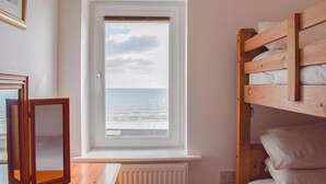 A room with a window overlooking the sea, a wooden bunk bed, and a radiator. - 3 bedroom accommodation in Sandown (Sandown)