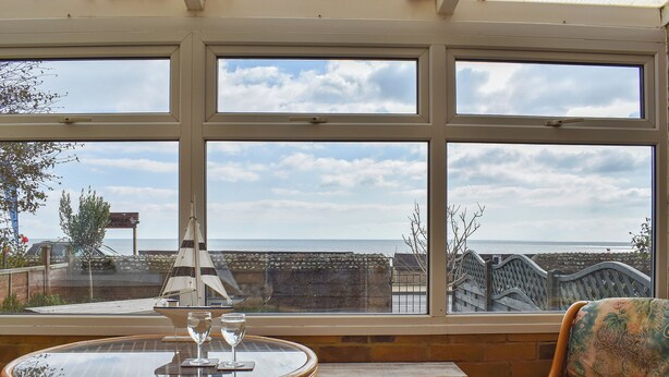 A room with a large window overlooking the sea, a wicker table with glasses, and a patterned chair. - 3 bedroom accommodation in Sandown (Sandown)