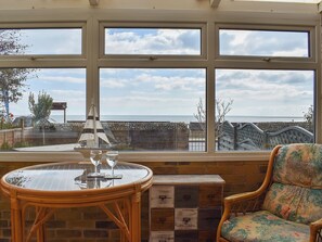 Ein Zimmer mit großem Meerblick, einem Korbstuhl und Gläsern sowie einem gemusterten Sessel.