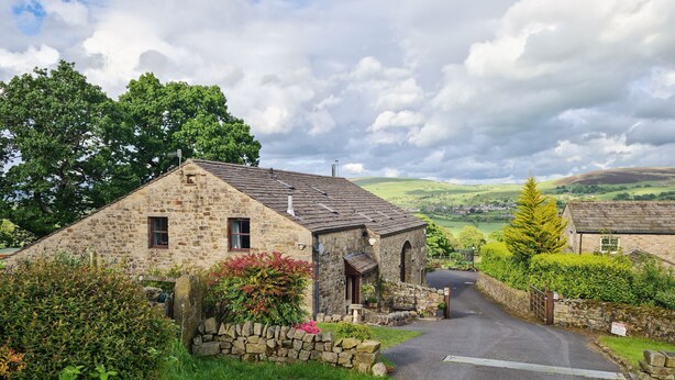A stone cottage with a paved driveway, surrounded by greenery and a rural landscape. - 3 bedroom accommodation in Salterforth, near Barnoldswick (Salterforth, near Barnoldswick)