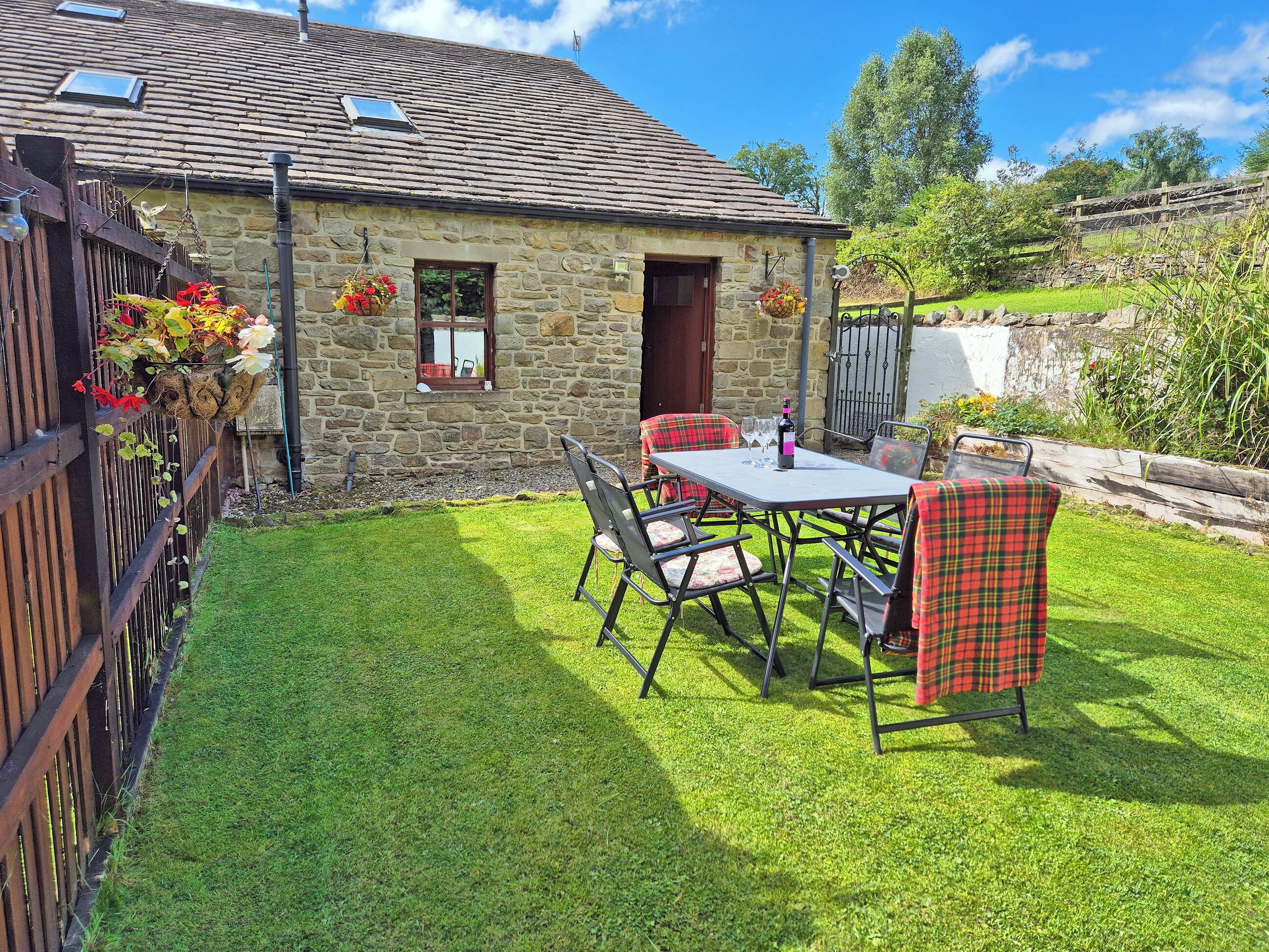 A stone house with a tiled roof, a fenced yard, and a table with chairs.