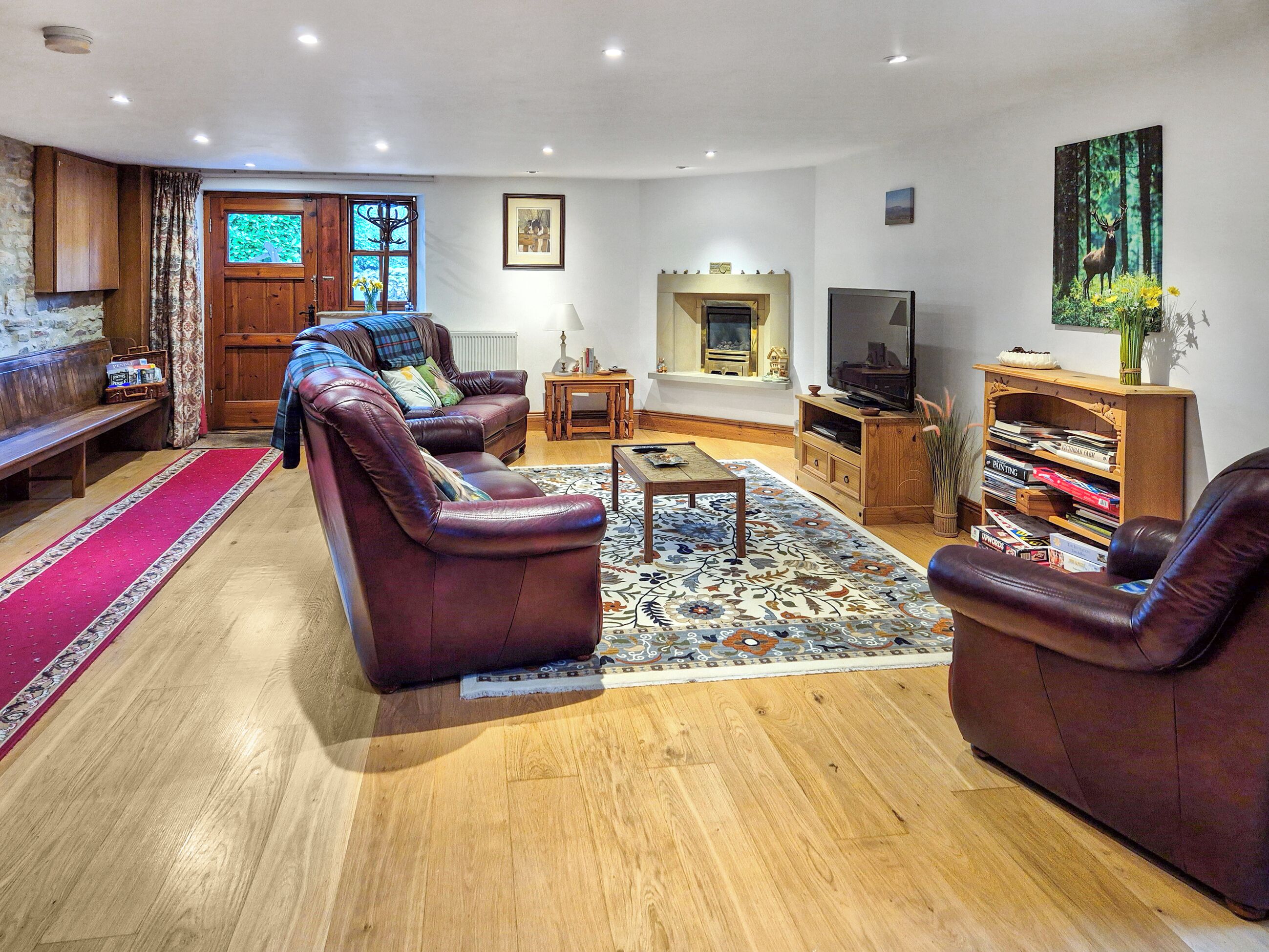 Een woonkamer met leren banken, een houten salontafel, een open haard, een televisie en een boekenplank.