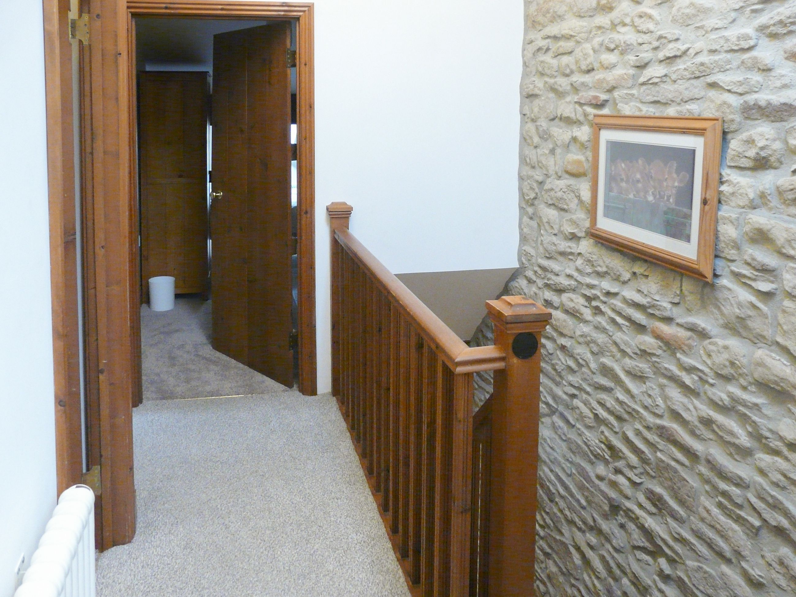 A hallway with a wooden railing, carpeted floor, and a stone wall with a framed picture.