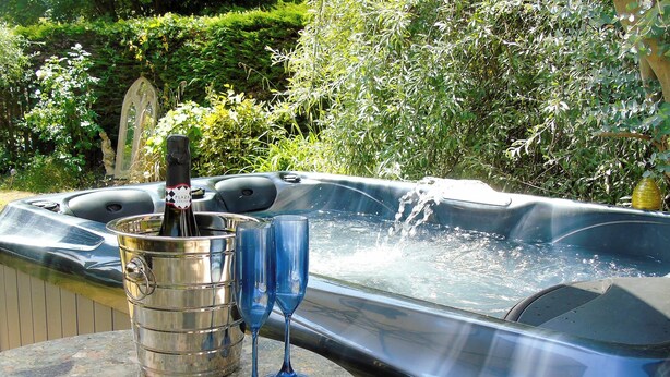 Un jacuzzi con una botella de champán y dos copas sobre una mesa de piedra.