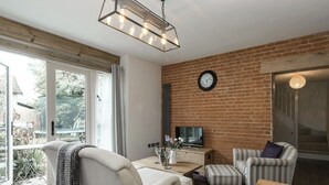 Una sala moderna con sofá, sillón, reposapiés, televisor y una pared de ladrillo con un reloj.