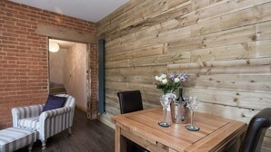 Una habitación acogedora con una pared de madera, una pared de ladrillo, un sofá a rayas, una pequeña mesa con un jarrón de flores y una silla.