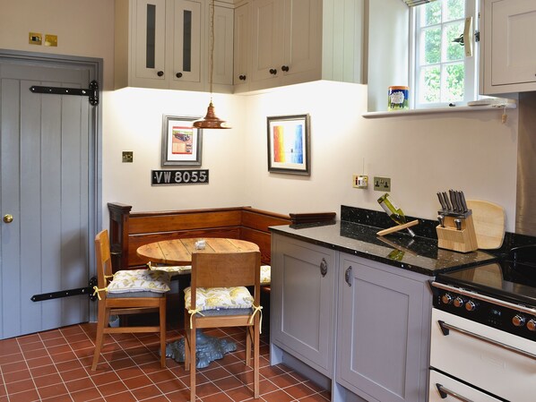 A kitchen with a wooden table and chairs, a stove, cabinets, and a window with a view of greenery.