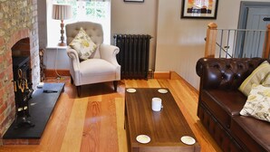 A living room with a fireplace, a wooden coffee table, a leather sofa, and a chair with a floral cushion. - The Coach House @ The Old Rectory (Buckland St Mary, near Chard)
