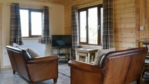 A wooden cabin interior with two leather sofas, a television on a stand, and large windows with plaid curtains. - 2 bedroom accommodation in Bromlow, near Minsterley (Bromlow, near Minsterley)