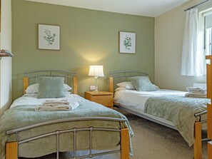 A twin bedroom with two beds, each with a nightstand, a lamp, and a framed botanical print on the wall.