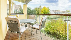 Een balkon met een tafel en stoelen, uitkijkend op een waterpartij en begroeiing.