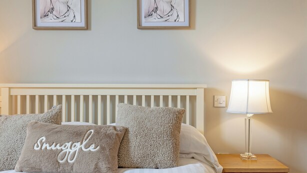 Een bed met gestreepte lakens, twee zachte kussens, een bedlampje en twee ingelijste kunstwerken aan de muur.