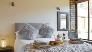 Un letto rifatto con cura, coperto da un piumone a motivi floreali, due cuscini soffici, un comodino con una lampada e un vassoio con asciugamani, croissant e teiera.