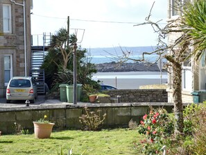 A residential area with a stone wall, a parked car, and a view of the sea.