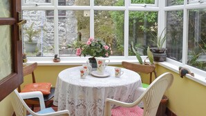 A room with a round table, two chairs, a window with a view of greenery, and a potted plant on the windowsill. - Most people have heard of St. (Marazion, near Penzance)