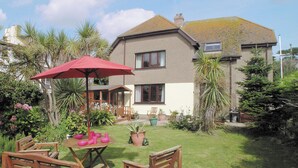 A house with a garden, a patio with wooden furniture, and a red umbrella. - Most people have heard of St. (Marazion, near Penzance)