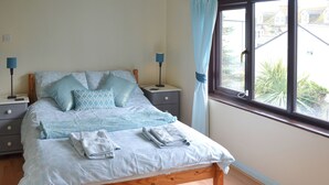 A neatly made bed with a wooden frame, a bedside table with a lamp, and a window with curtains. - Most people have heard of St. (Marazion, near Penzance)