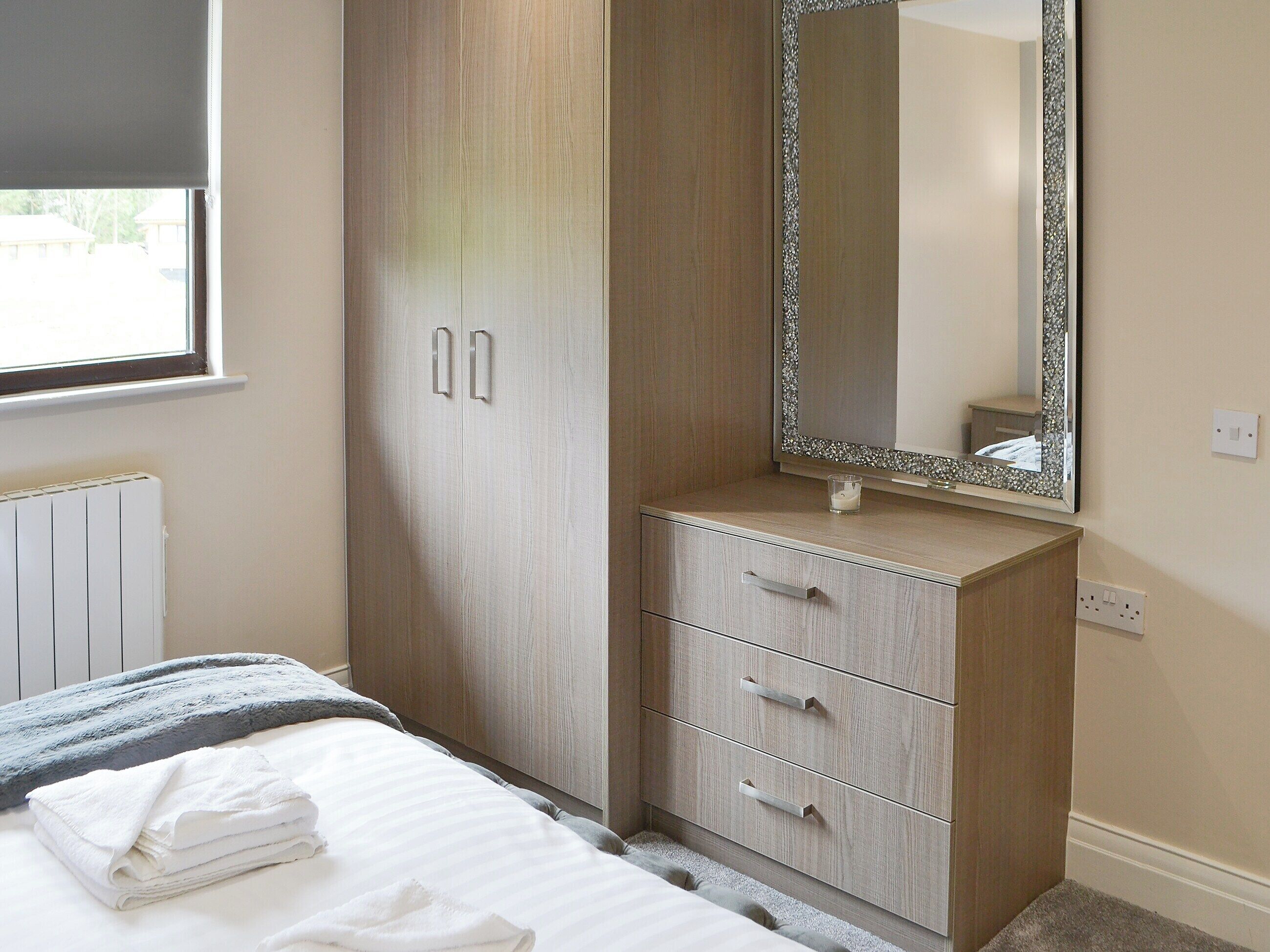 Un dormitorio con cama, armario de dos puertas, espejo y radiador.