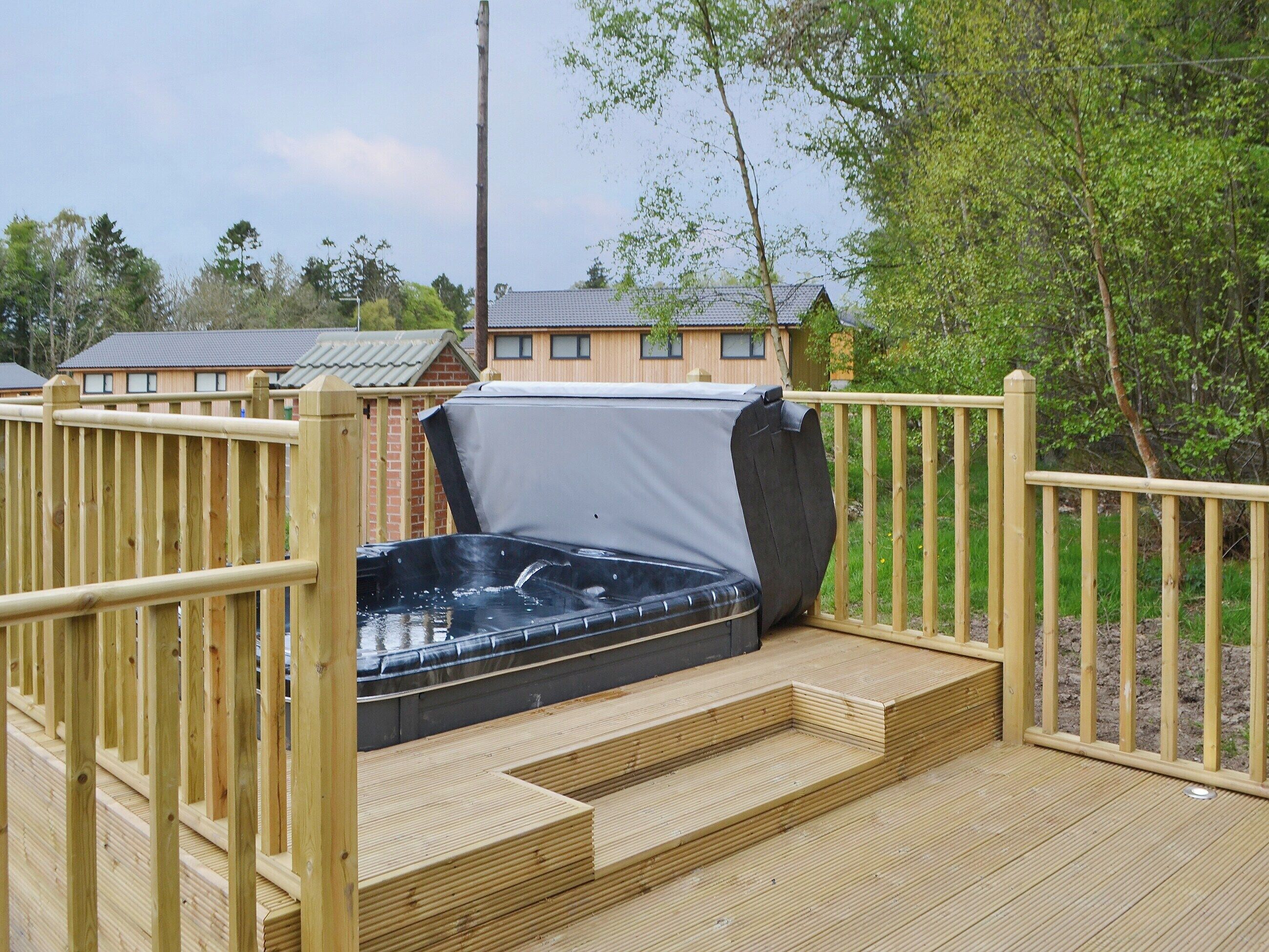 A hot tub on a wooden deck with a wooden fence surrounding it.
