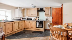 A modern kitchen with wooden cabinets, a gas stove, and a dining area with wooden chairs. - 1 bedroom accommodation in Elsdon (Elsdon)