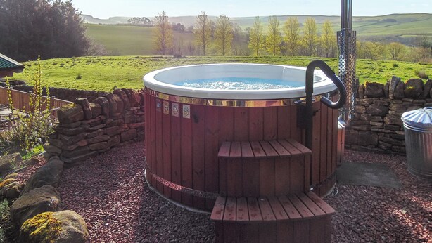 A hot tub with a wooden exterior, surrounded by a stone wall and gravel. - 1 bedroom accommodation in Elsdon (Elsdon)