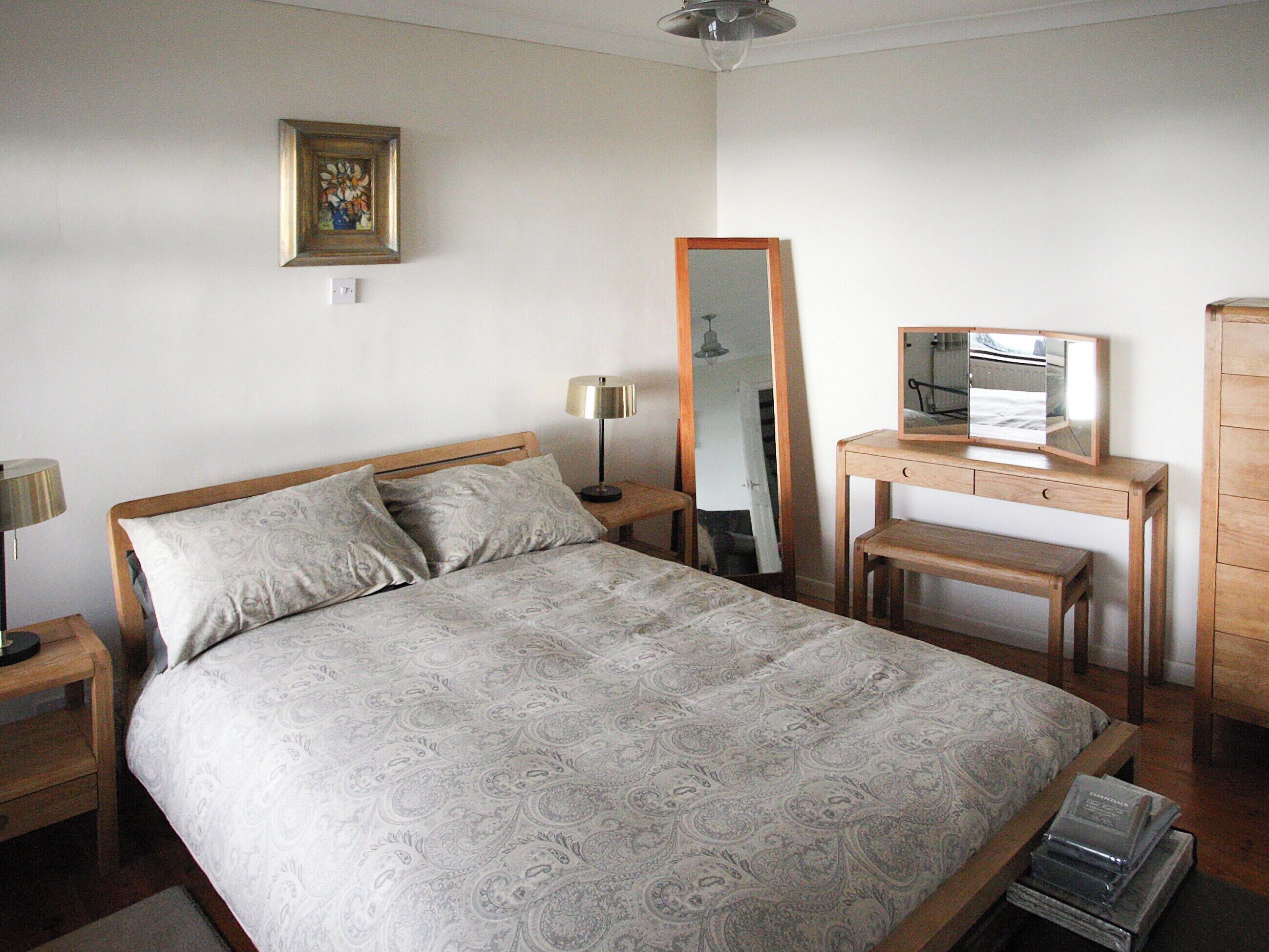 Une chambre à coucher comprenant un lit, une table de chevet, une commode, un miroir et un bureau.