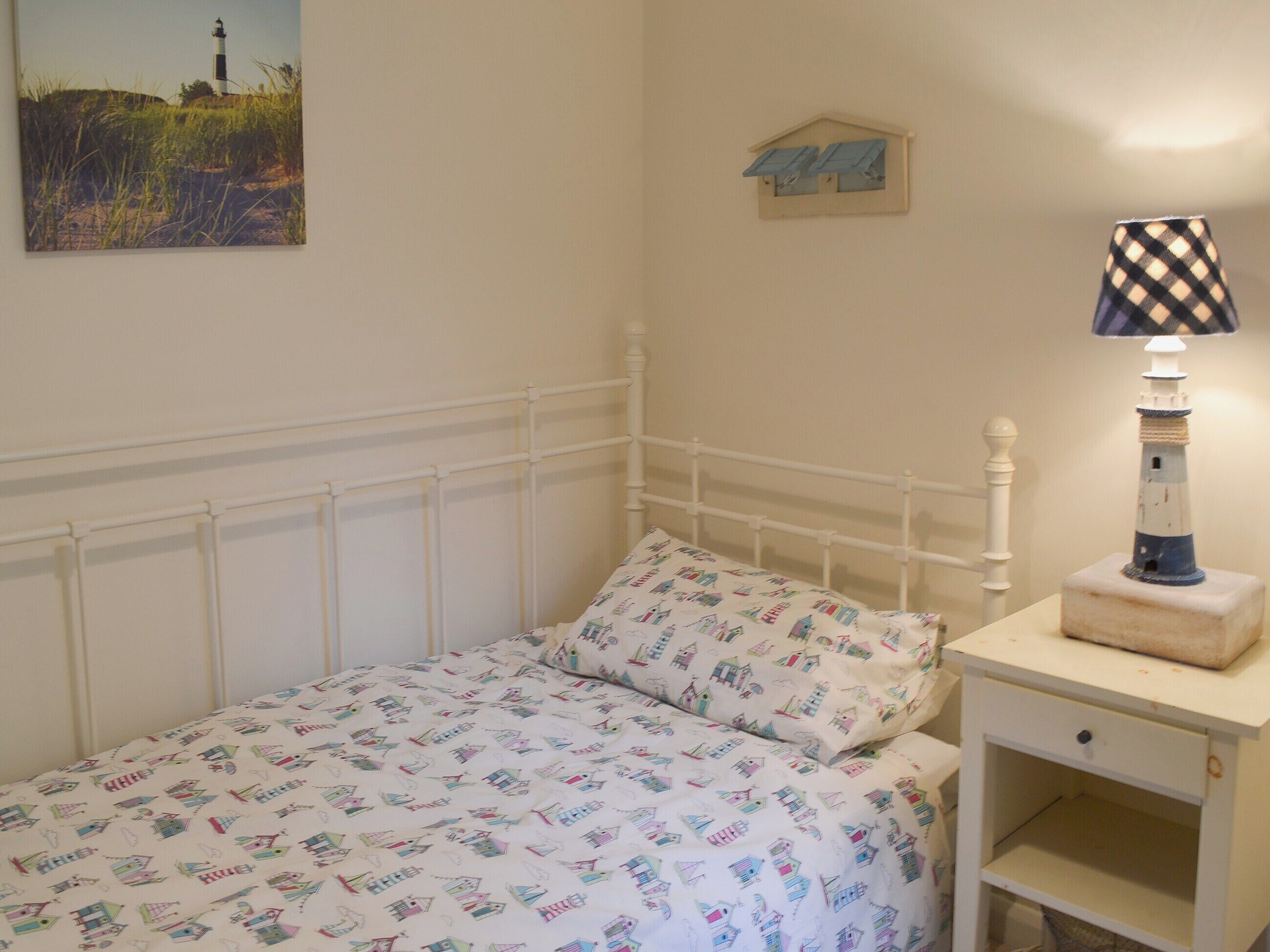 Un dormitorio con cama, mesita de noche, lámpara y estante en la pared.