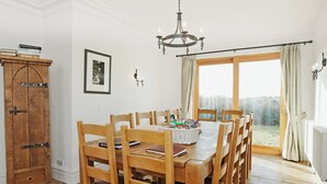 Een eetkamer met een houten tafel en stoelen, een kroonluchter, een houten kast en een raam met gordijnen.