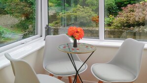 A corner with two white chairs and a small round table with a glass top, placed near a window overlooking a garden. - 2 bedroom accommodation in Cockermouth (Cockermouth)