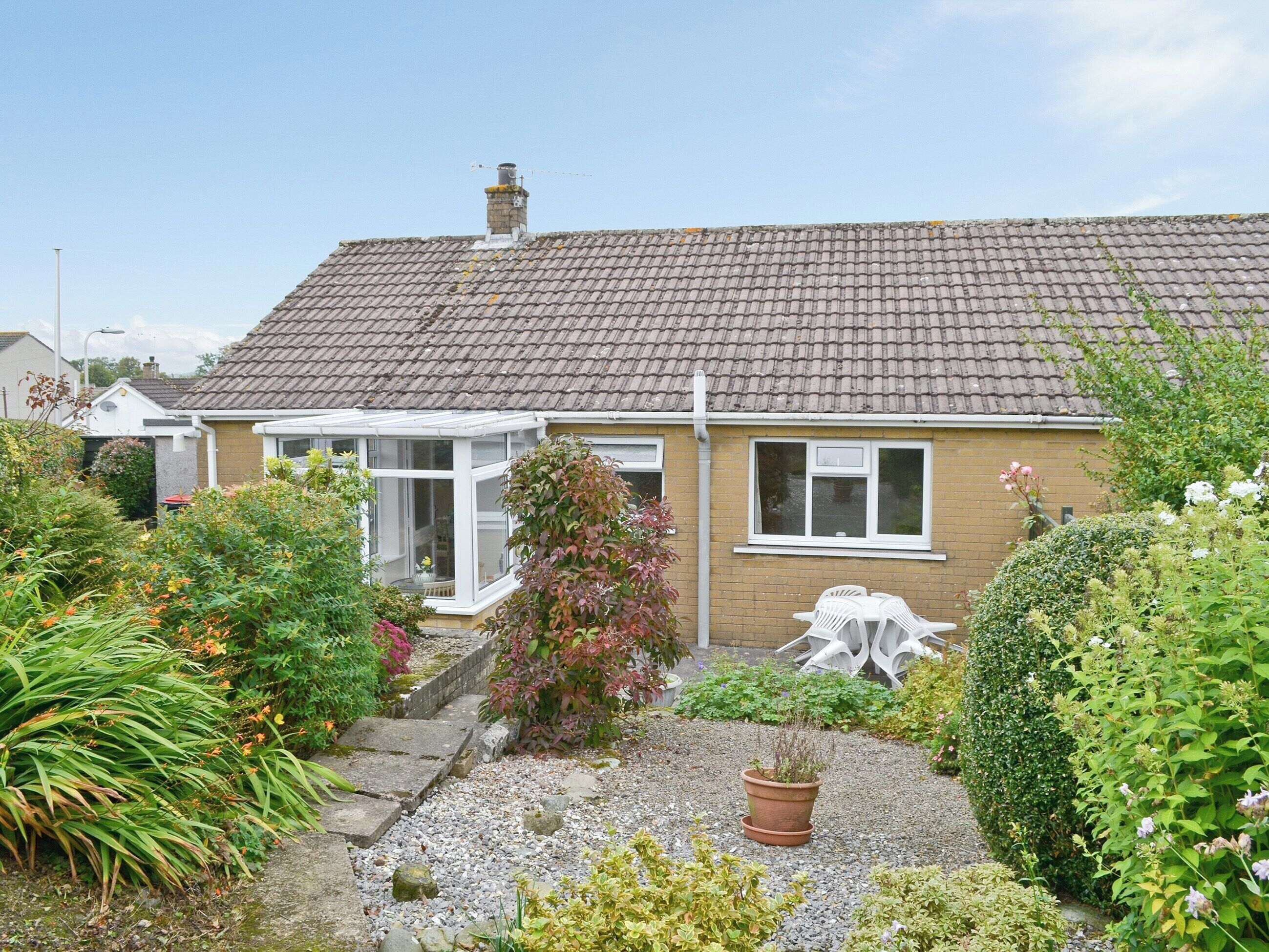 A house with a tiled roof, a conservatory, and a garden with various plants and a gravel path.
