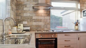 A kitchen with a stone backsplash, stainless steel appliances, a window with blinds, and a view of the outdoors. - 2 bedroom accommodation in Cockermouth (Cockermouth)