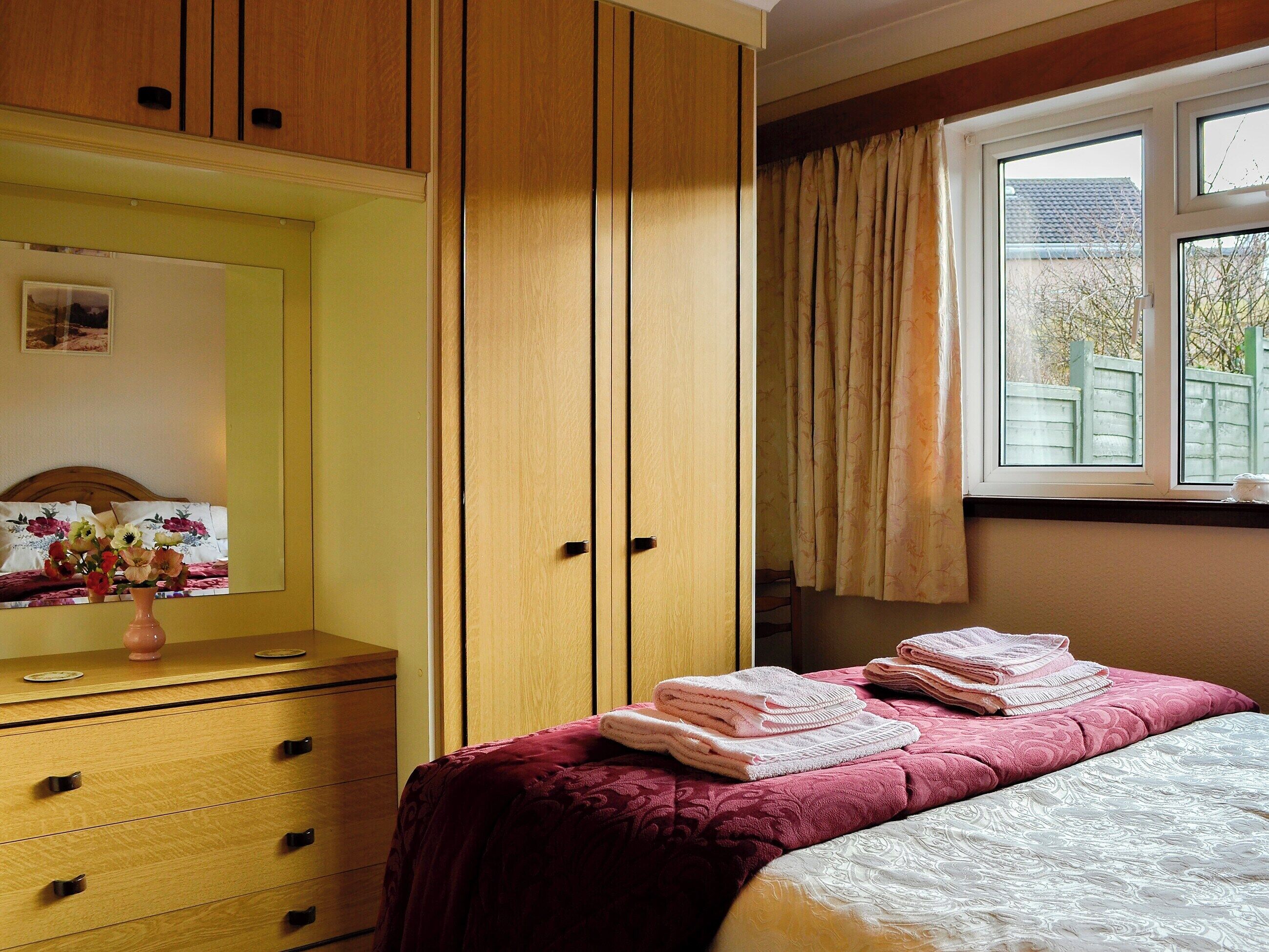 Ein Schlafzimmer mit Bett, Kommode, Spiegel und einem Fenster mit Vorhängen.
