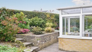 A garden with a variety of plants and a small conservatory with a table and chairs. - 2 bedroom accommodation in Cockermouth (Cockermouth)