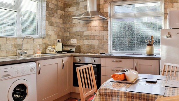 A compact kitchen with a built-in oven, a washing machine, and a dining area with a table and chairs. - 2 bedroom accommodation in Cockermouth (Cockermouth)