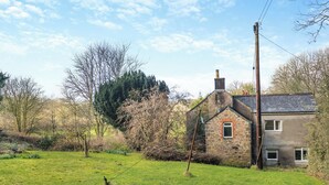 A stone house with a chimney, surrounded by a grassy field and trees. - 2 bedroom accommodation in Harford, Dartmoor National Park (Harford, Dartmoor National Park)