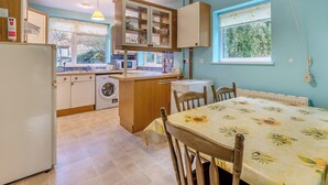 A kitchen with a washing machine, a dining table with chairs, and a window with a view of greenery. - 2 bedroom accommodation in Harford, Dartmoor National Park (Harford, Dartmoor National Park)